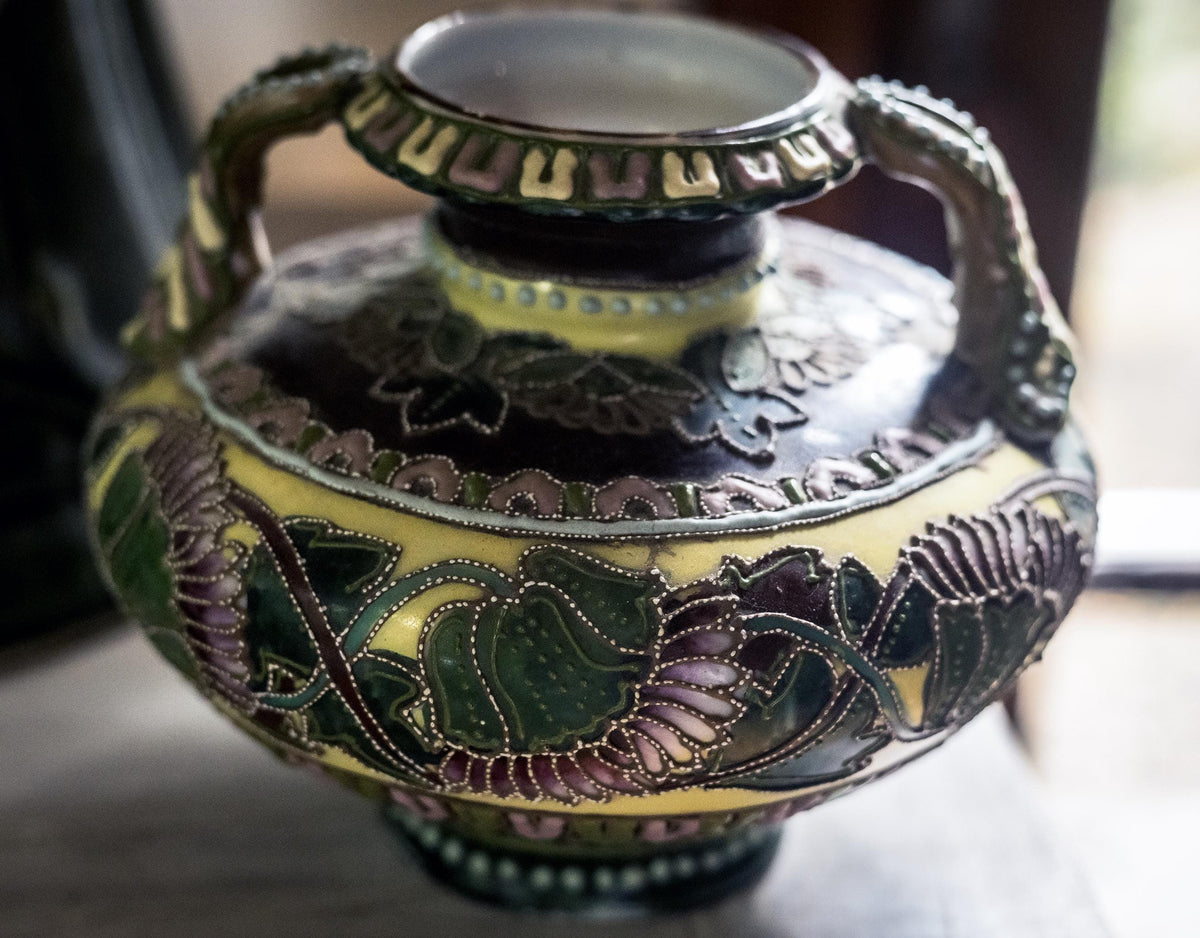 An ornate vintage ceramic vase with a dark brown and yellow floral pattern, featuring green and purple enamel details and decorative handles.